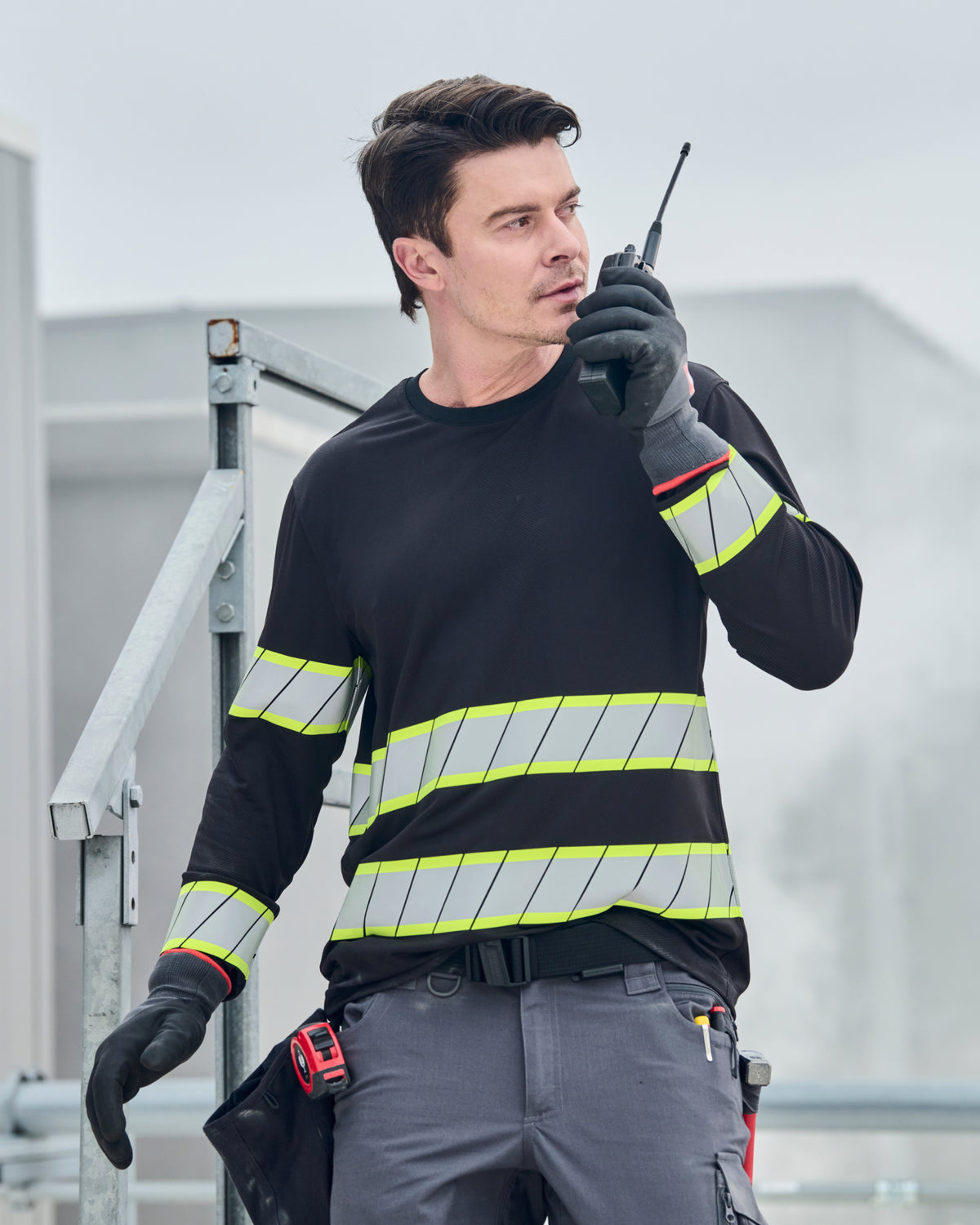 A worker wears the STRAUSS Enhanced Visibility Long Sleeve Shirt in black with dark work pants near construction equipment