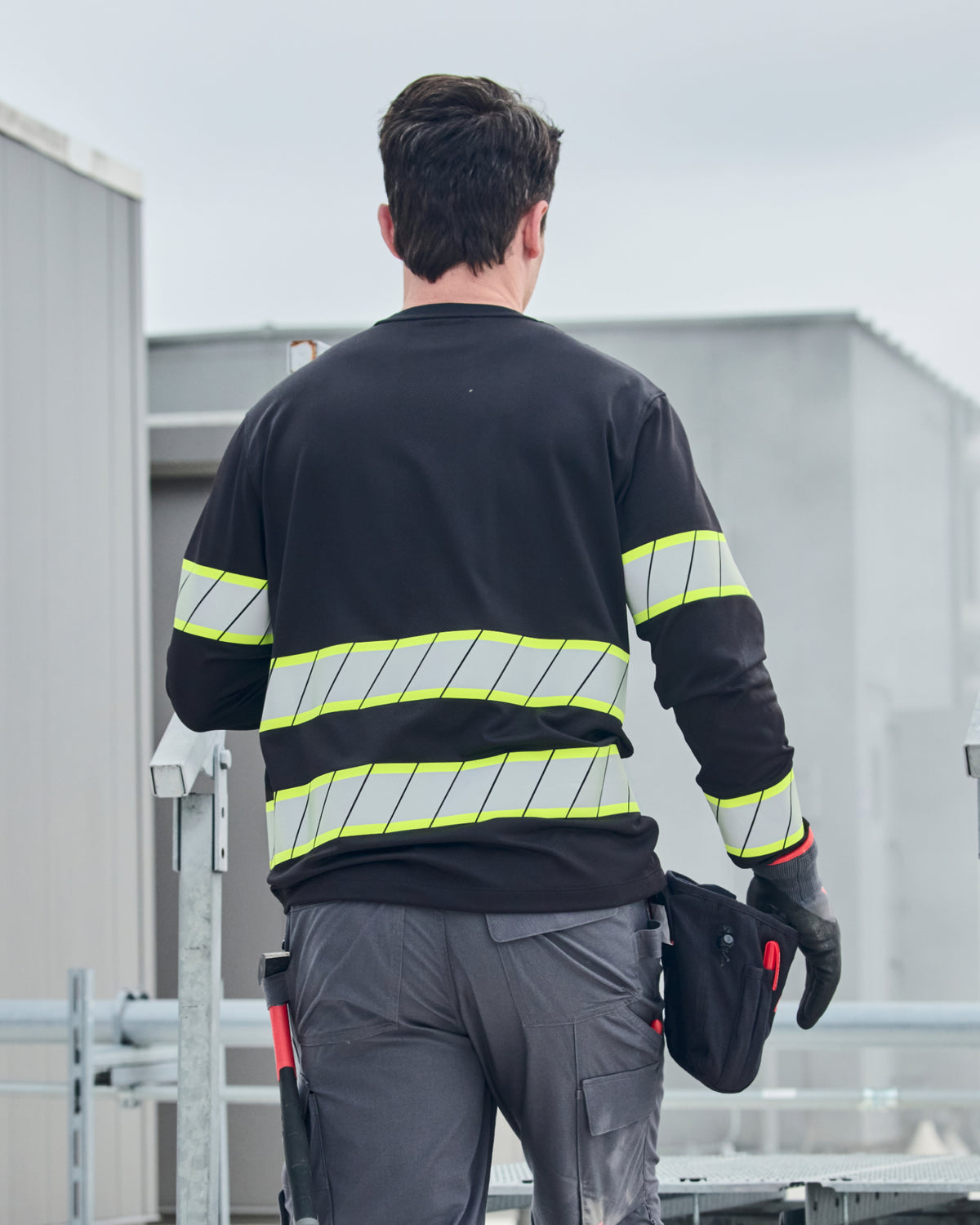 A worker wears the STRAUSS Enhanced Visibility Long Sleeve Shirt in black with work pants while handling materials at a jobsite