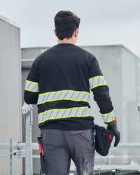 A worker wears the STRAUSS Enhanced Visibility Long Sleeve Shirt in black with work pants while handling materials at a jobsite
