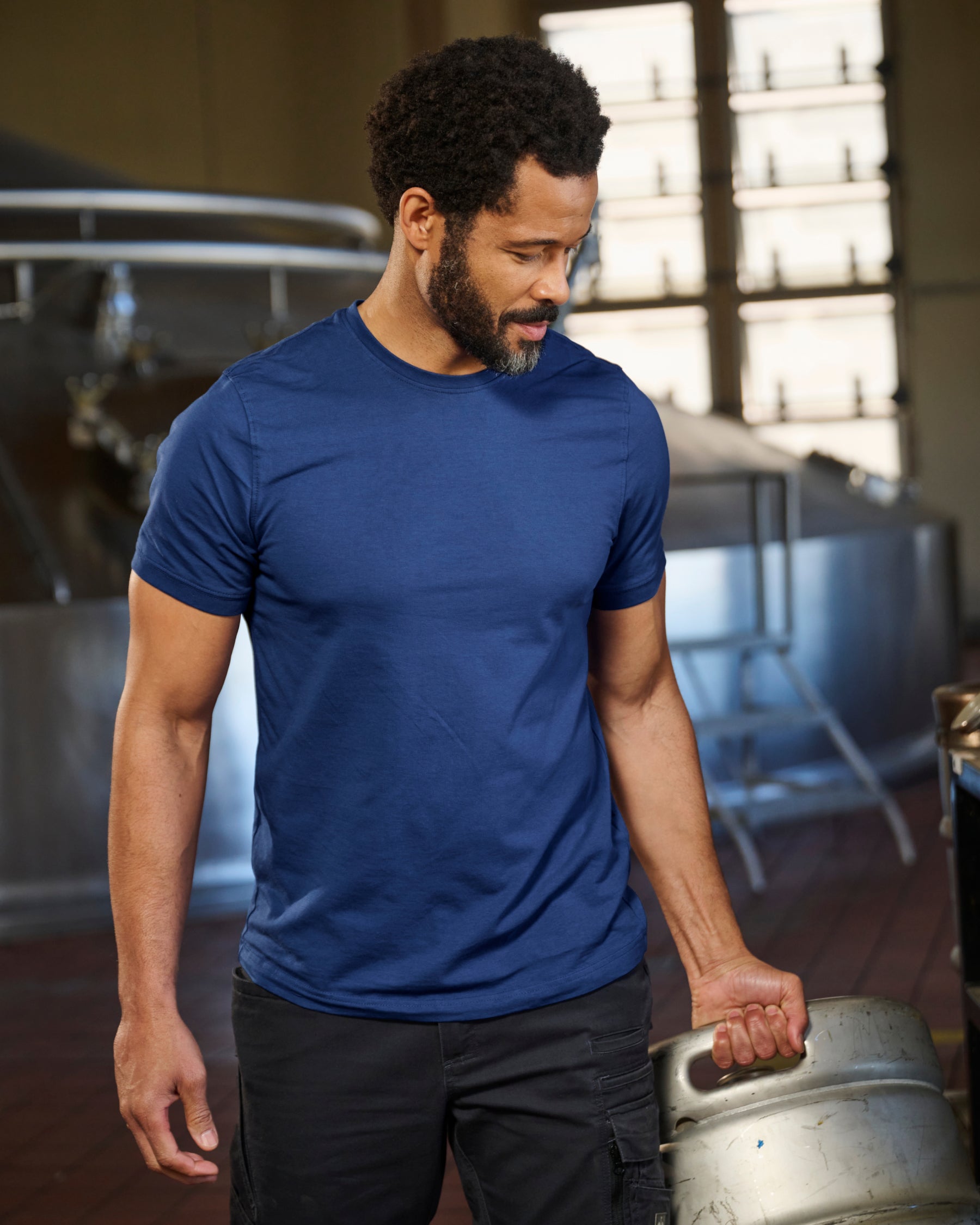 A worker wears the STRAUSS Cotton Stretch T-Shirt in alkali blue with tan work pants on a jobsite