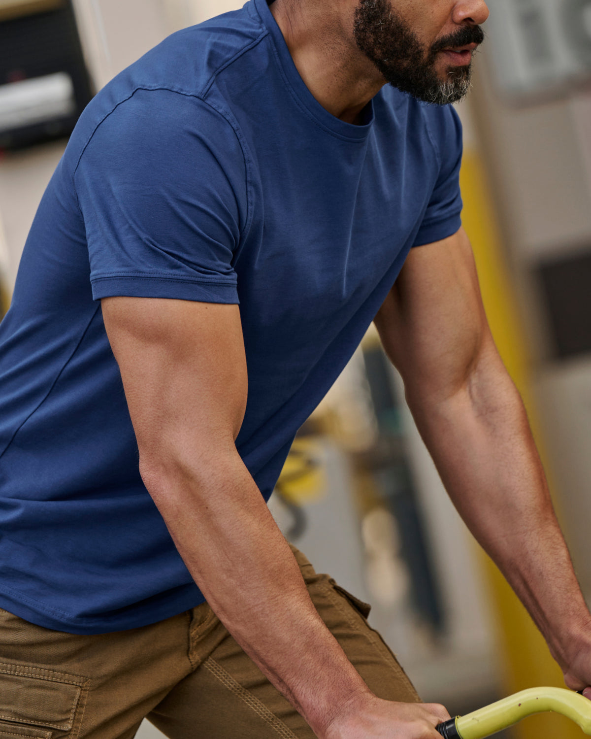 A worker wears the STRAUSS Cotton Stretch T-Shirt in alkali blue with tan work pants beside jobsite equipment