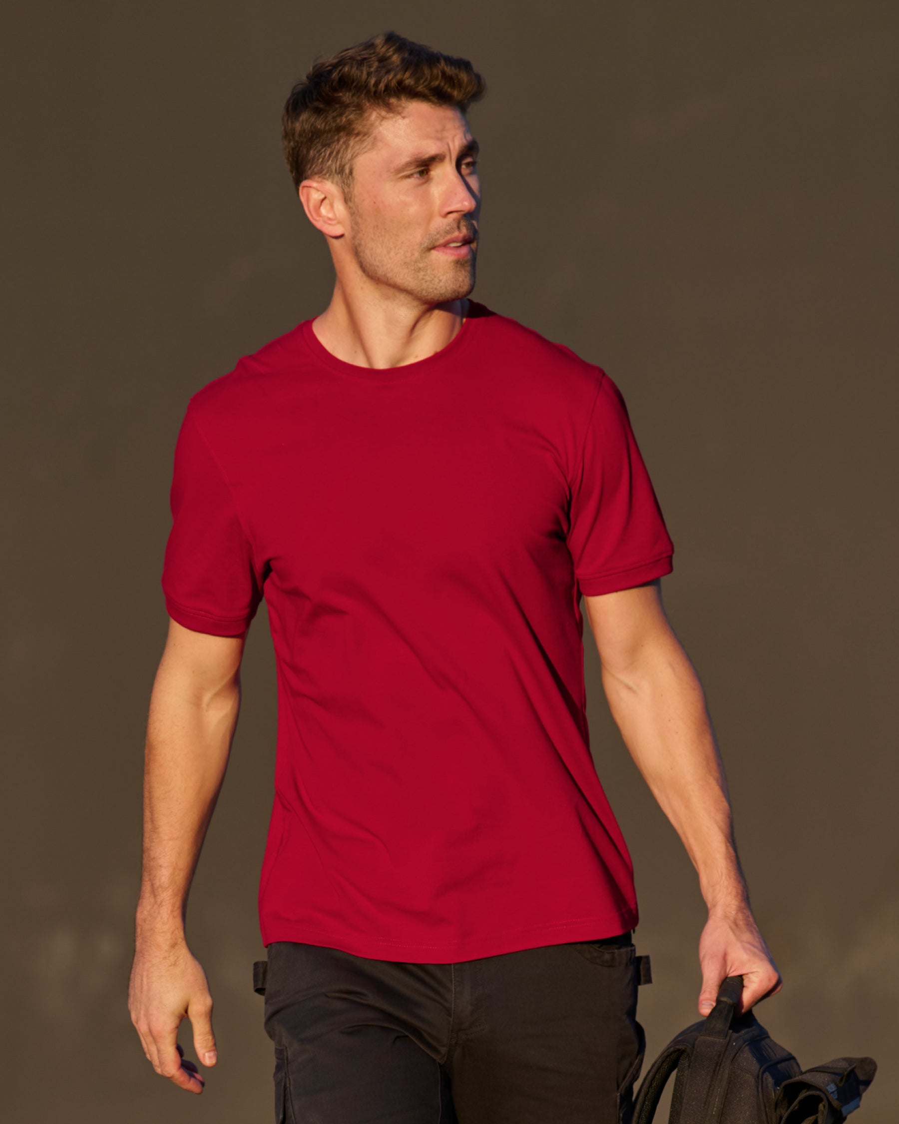 A worker wears the STRAUSS Cotton Stretch T-Shirt in fire red with black work pants on a sunny jobsite