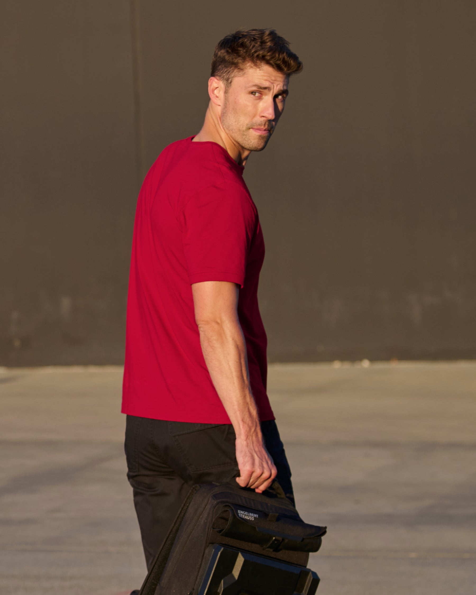 A worker wears the STRAUSS Cotton Stretch T-Shirt in fire red with black work pants while working