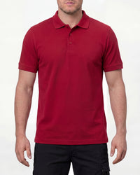 A model wears the STRAUSS Cotton Stretch Polo Shirt in fire red with tan work pants and work boots in a studio product scene