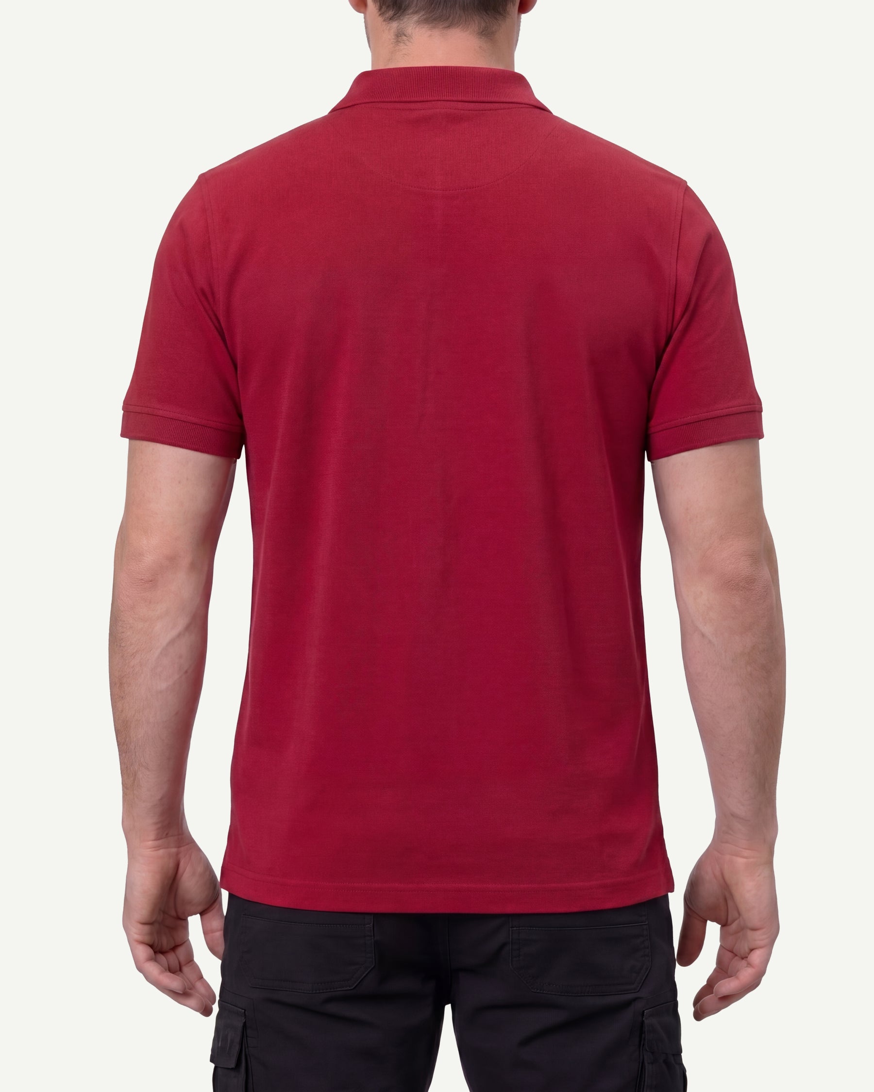 A model wears the STRAUSS Cotton Stretch Polo Shirt in fire red with tan work pants and work boots, showing the shirt fit