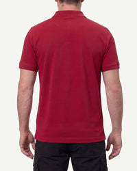 A model wears the STRAUSS Cotton Stretch Polo Shirt in fire red with tan work pants and work boots, showing the shirt fit
