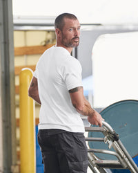 A worker wears the STRAUSS Cotton Stretch T-Shirt in white with tan work pants while working in a field