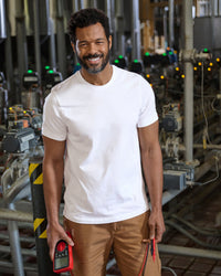 A worker wears the STRAUSS Cotton Stretch T-Shirt in white with tan work pants beside jobsite equipment