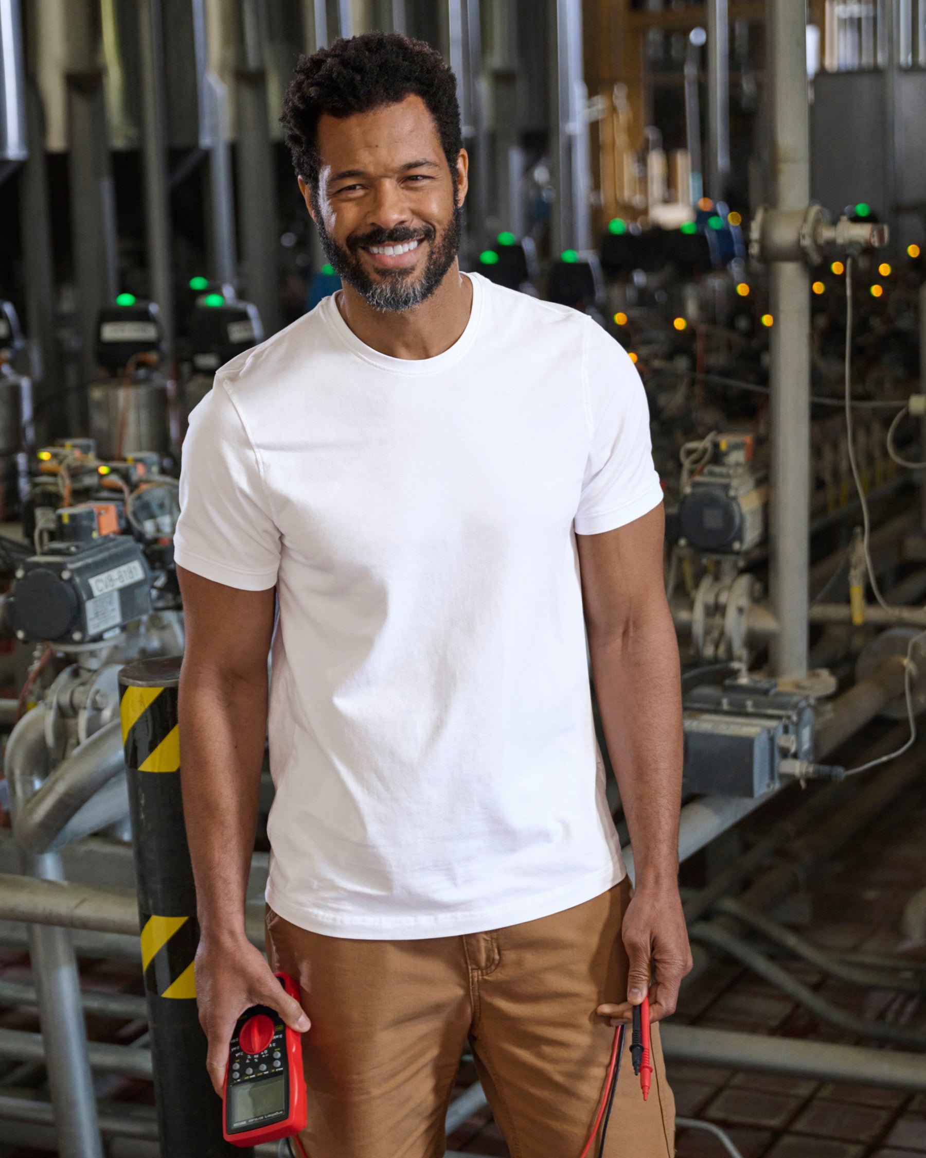 A worker wears the STRAUSS Cotton Stretch T-Shirt in white with tan work pants beside jobsite equipment