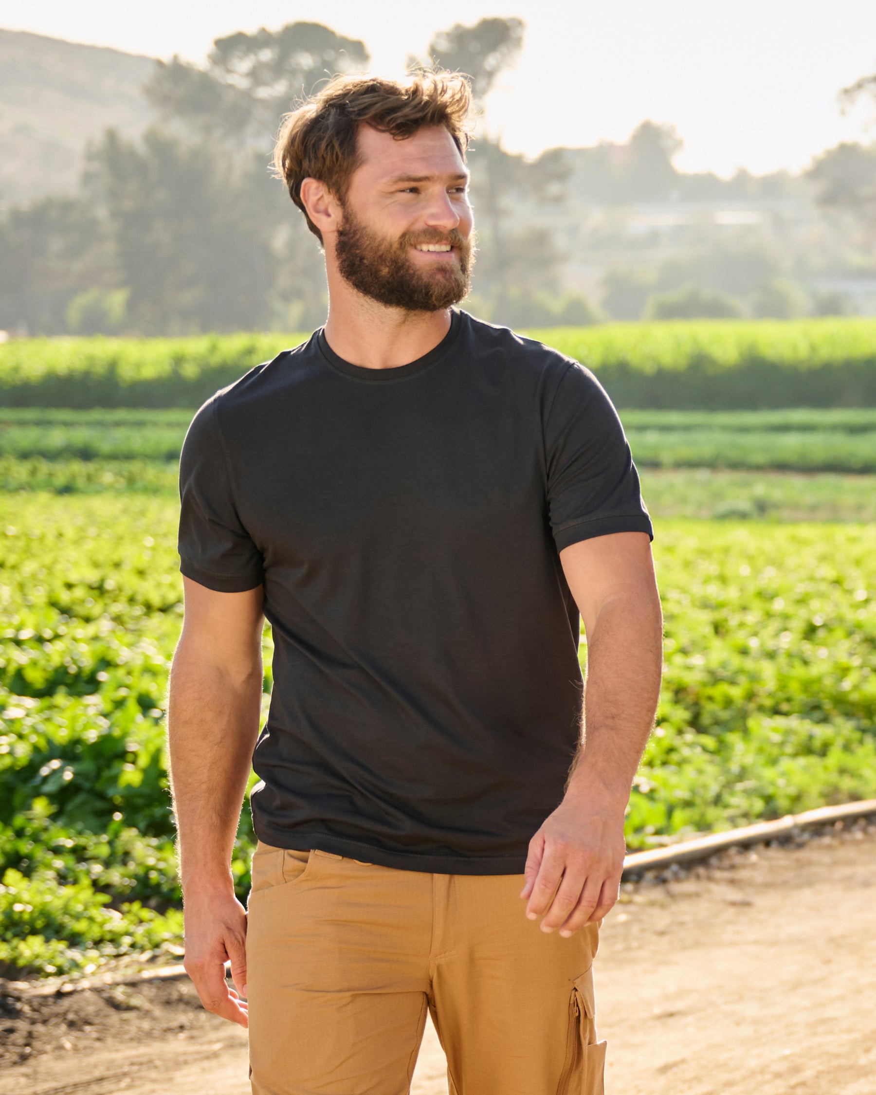 A worker wears the STRAUSS Cotton Stretch T-Shirt in black with tan work pants while working in a field