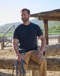 A worker wears the STRAUSS Cotton Stretch T-Shirt in black with tan work pants beside jobsite equipment