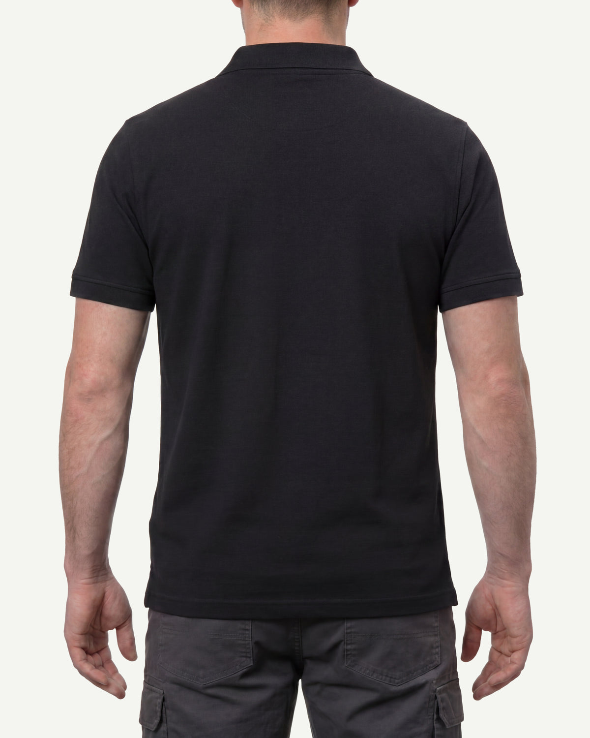 A model wears the STRAUSS Cotton Stretch Polo Shirt in black with tan work pants and work boots, showing the shirt fit