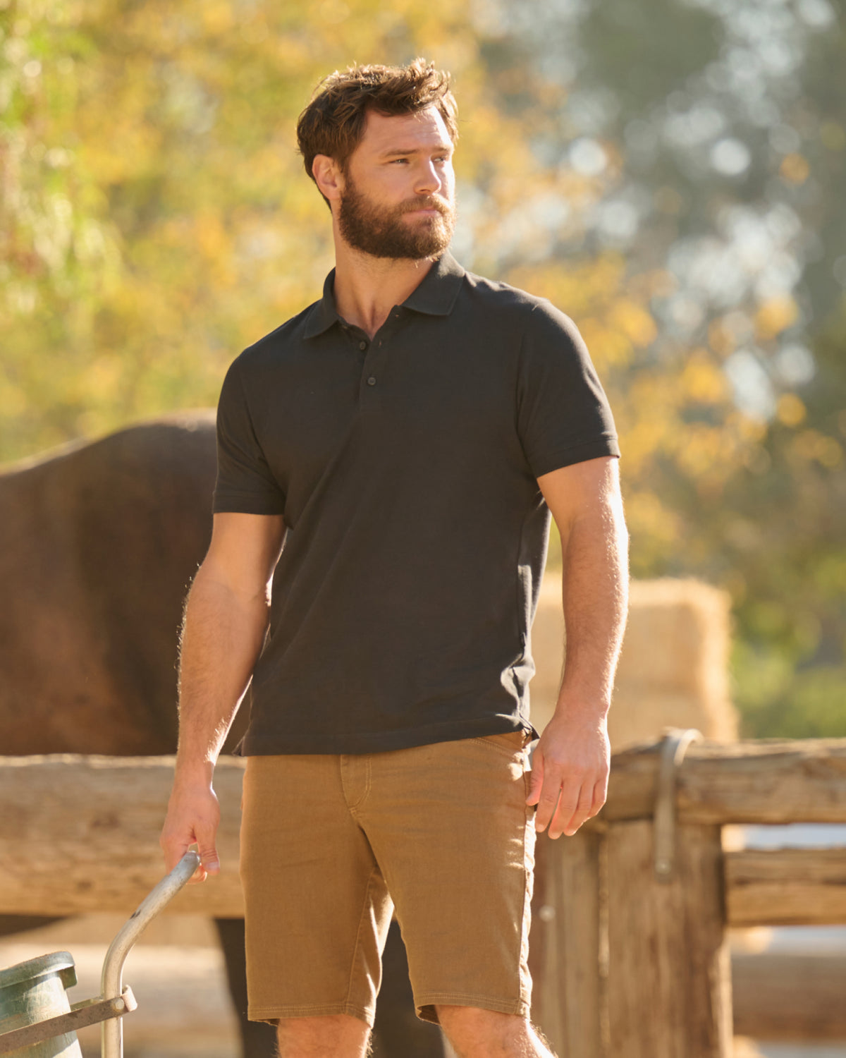 A worker wears the STRAUSS Cotton Stretch Polo Shirt in black with tan work pants on a sunny jobsite