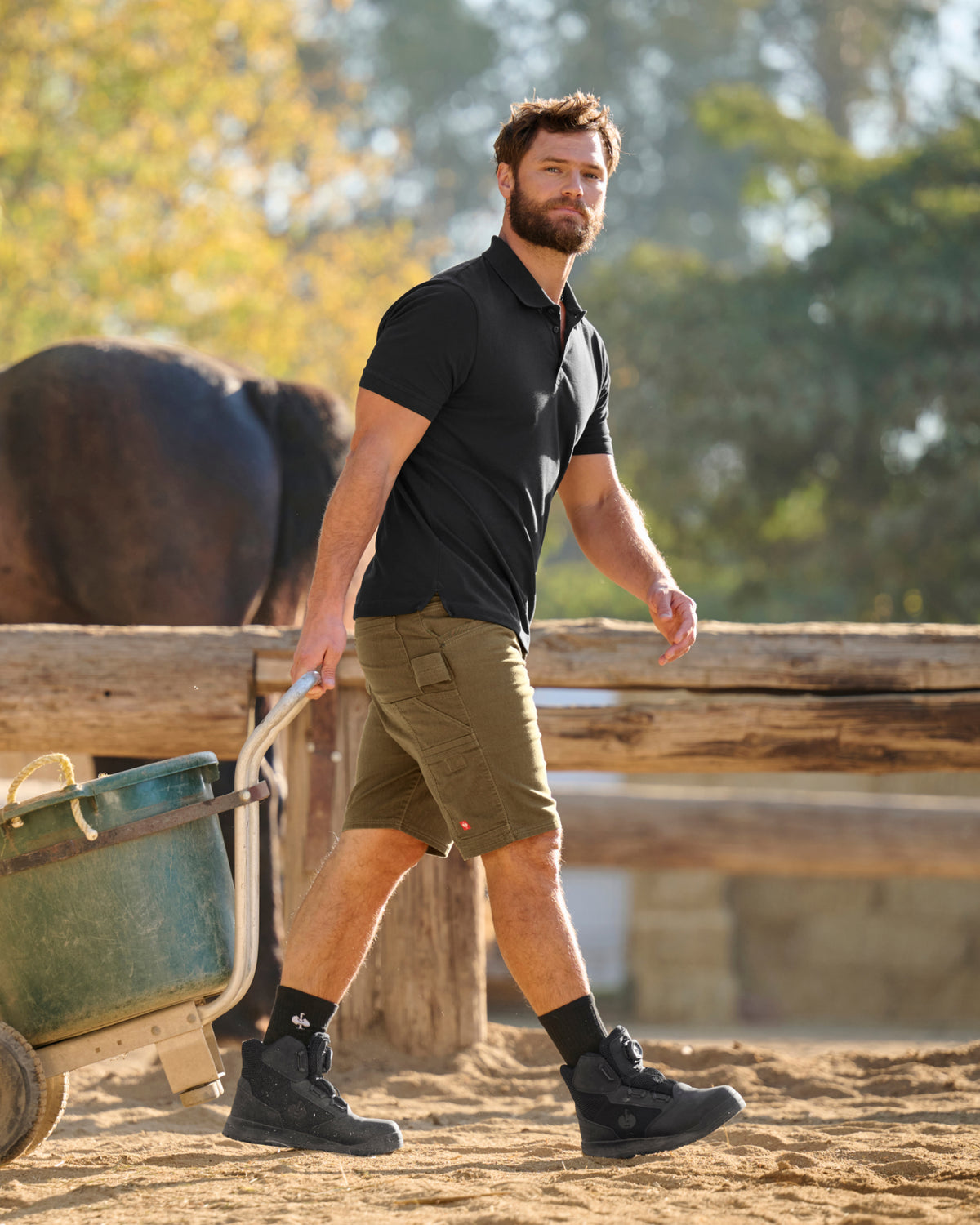 A worker wears the STRAUSS Cotton Stretch Polo Shirt in black with tan work pants while working in a field