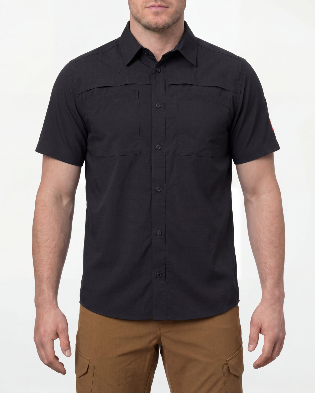 A model wears the STRAUSS e.s.taktik Stretch Ripstop Short Sleeve Work Shirt in black open over a T-shirt with work pants and work boots in a studio product scene