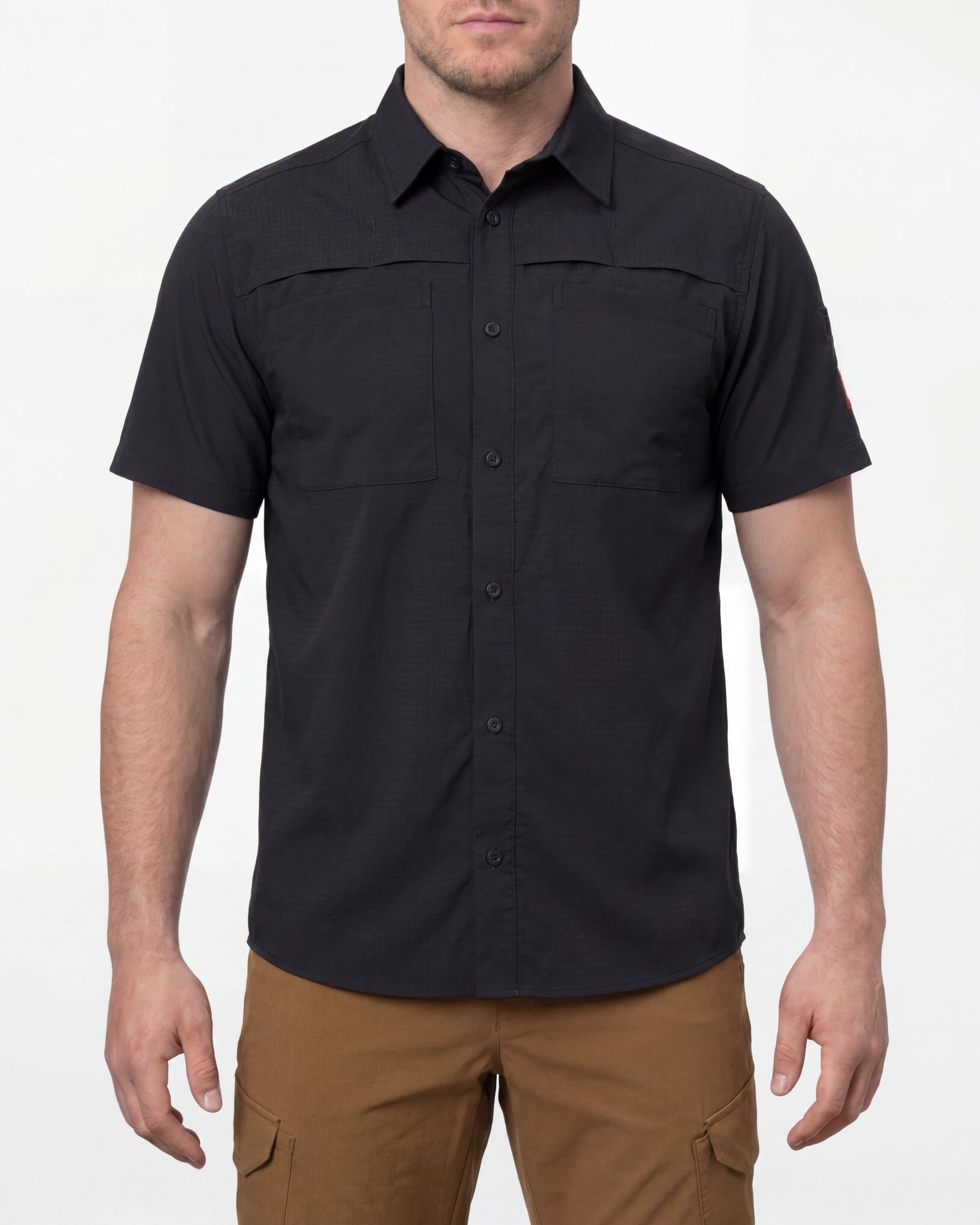 A model wears the STRAUSS e.s.taktik Stretch Ripstop Short Sleeve Work Shirt in black open over a T-shirt with work pants and work boots in a studio product scene