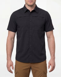 A model wears the STRAUSS e.s.taktik Stretch Ripstop Short Sleeve Work Shirt in black open over a T-shirt with work pants and work boots in a studio product scene