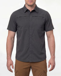 A model wears the STRAUSS e.s.taktik Stretch Ripstop Short Sleeve Work Shirt in carbon gray open over a T-shirt with work pants and work boots in a studio product scene
