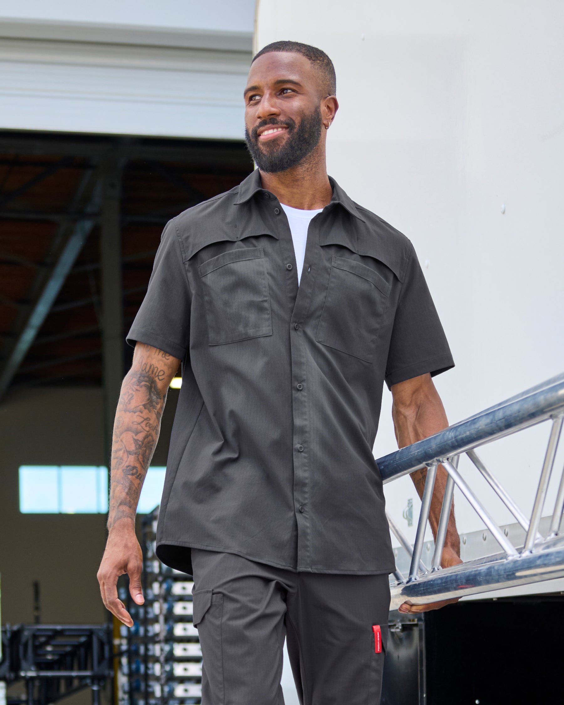 A worker wears the STRAUSS e.s.taktik Stretch Ripstop Short Sleeve Work Shirt in carbon gray over a T-shirt with cargo work pants at a jobsite
