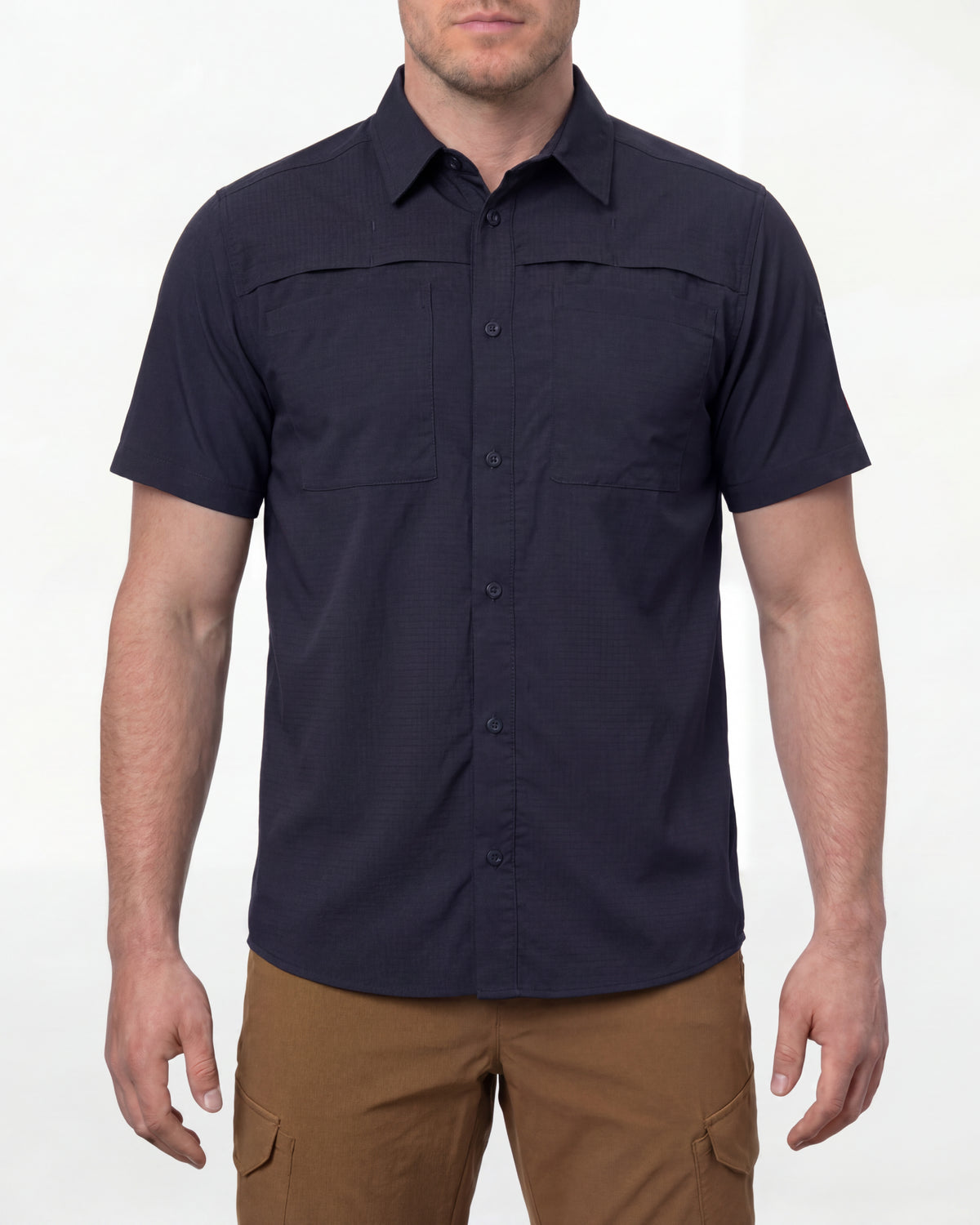 A model wears the STRAUSS e.s.taktik Stretch Ripstop Short Sleeve Work Shirt in nero blue open over a T-shirt with work pants and work boots in a studio product scene