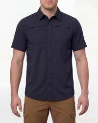 A model wears the STRAUSS e.s.taktik Stretch Ripstop Short Sleeve Work Shirt in nero blue open over a T-shirt with work pants and work boots in a studio product scene