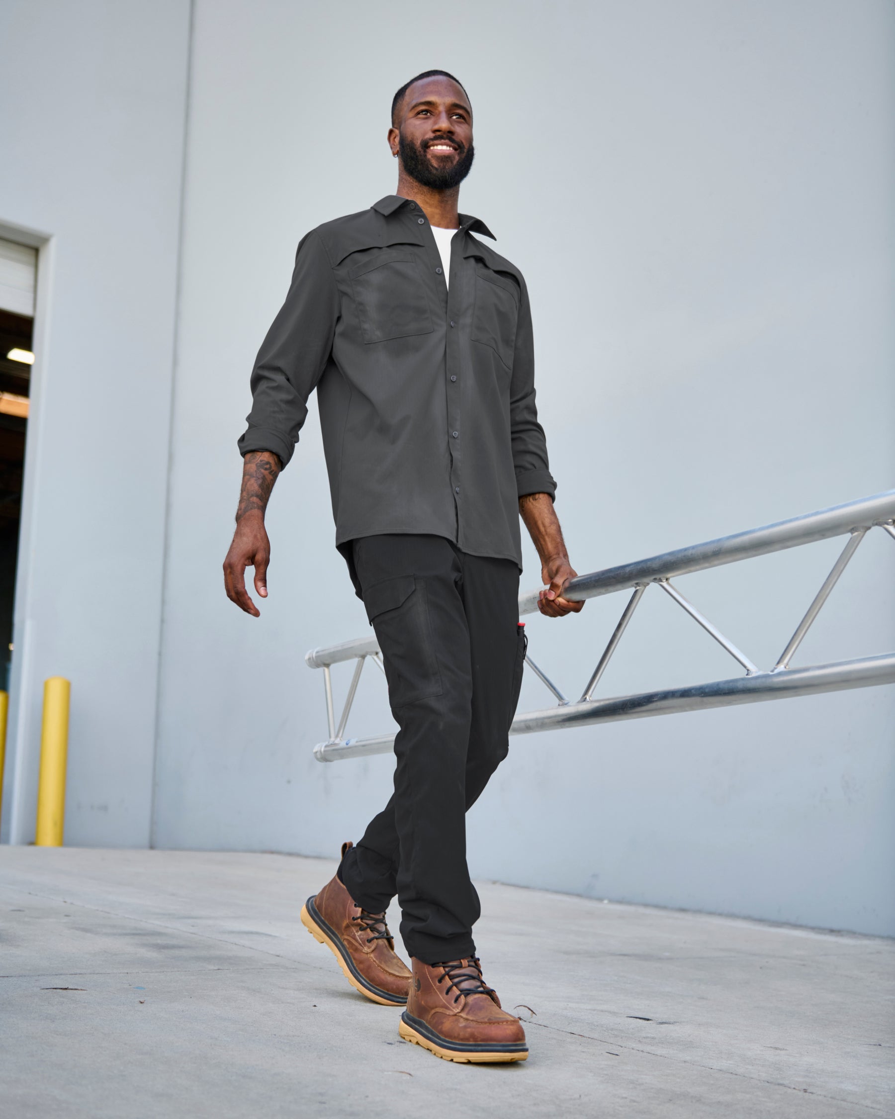 A worker wears the STRAUSS e.s.taktik Stretch Ripstop Long Sleeve Work Shirt in carbon gray over a T-shirt with cargo work pants at a jobsite