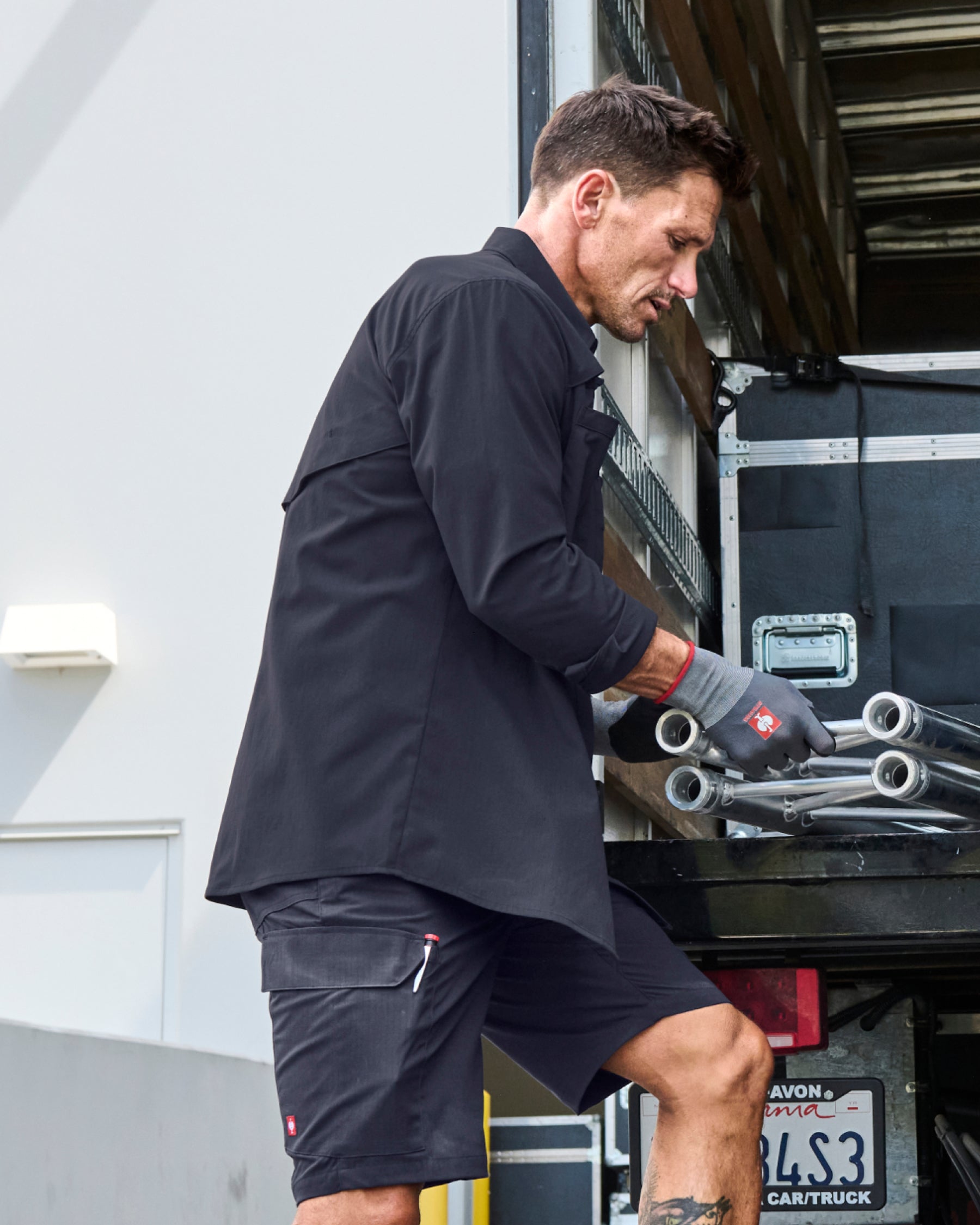 A worker wears the STRAUSS e.s.taktik Stretch Ripstop Long Sleeve Work Shirt in nero blue while moving materials beside metal shelving