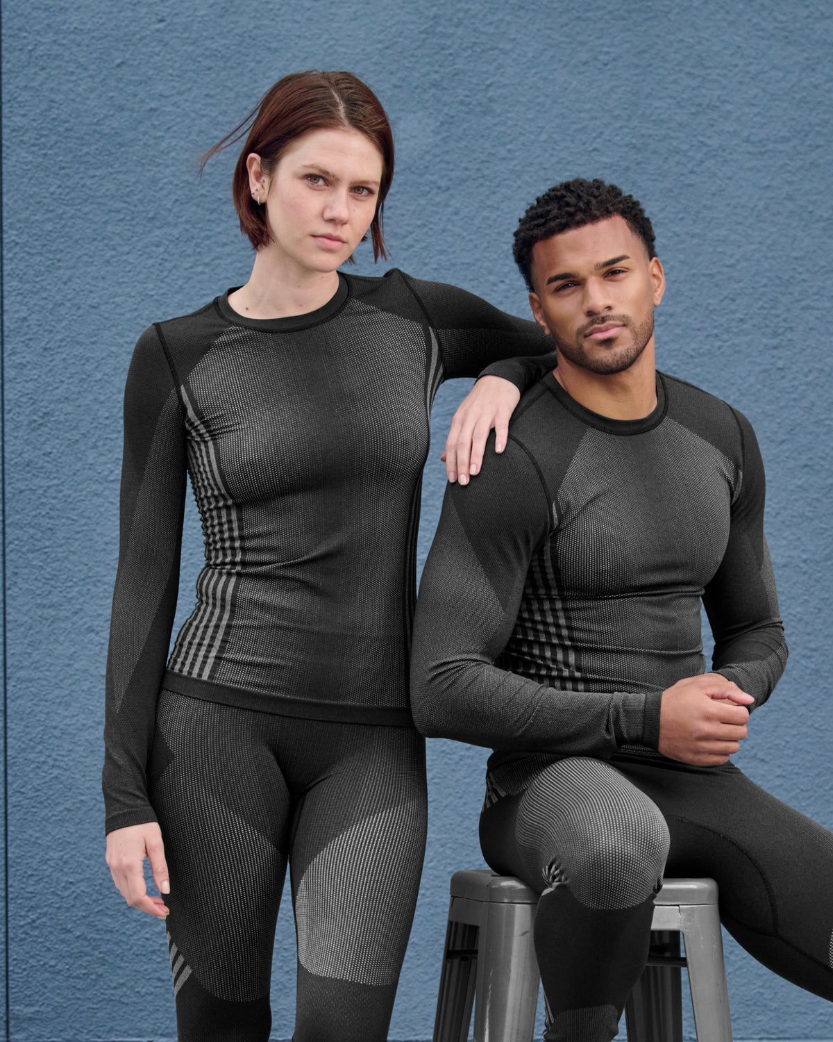 A woman wears the Women's STRAUSS e.s.trail pure Warm Seamless Thermal Long Sleeve Shirt in black and basalt gray as a base layer