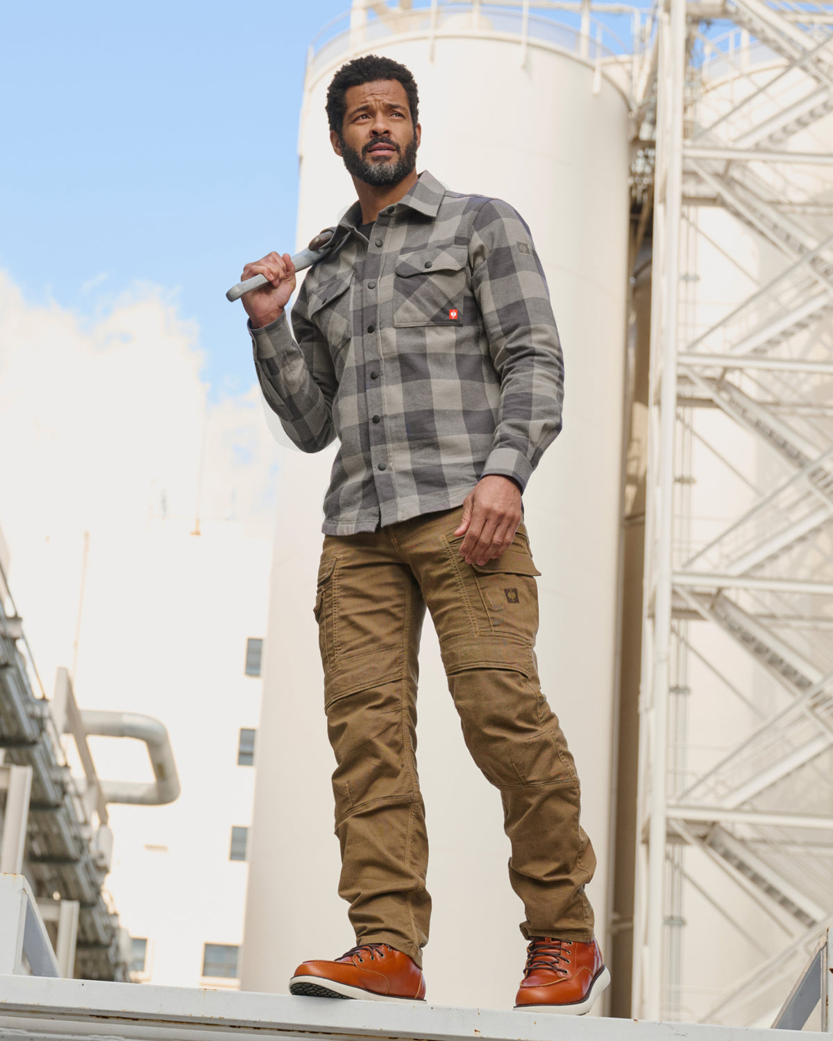 A worker wears the STRAUSS e.s.iconic Flannel Work Shirt in dolphin gray and carbon gray over a T-shirt with work pants on a jobsite