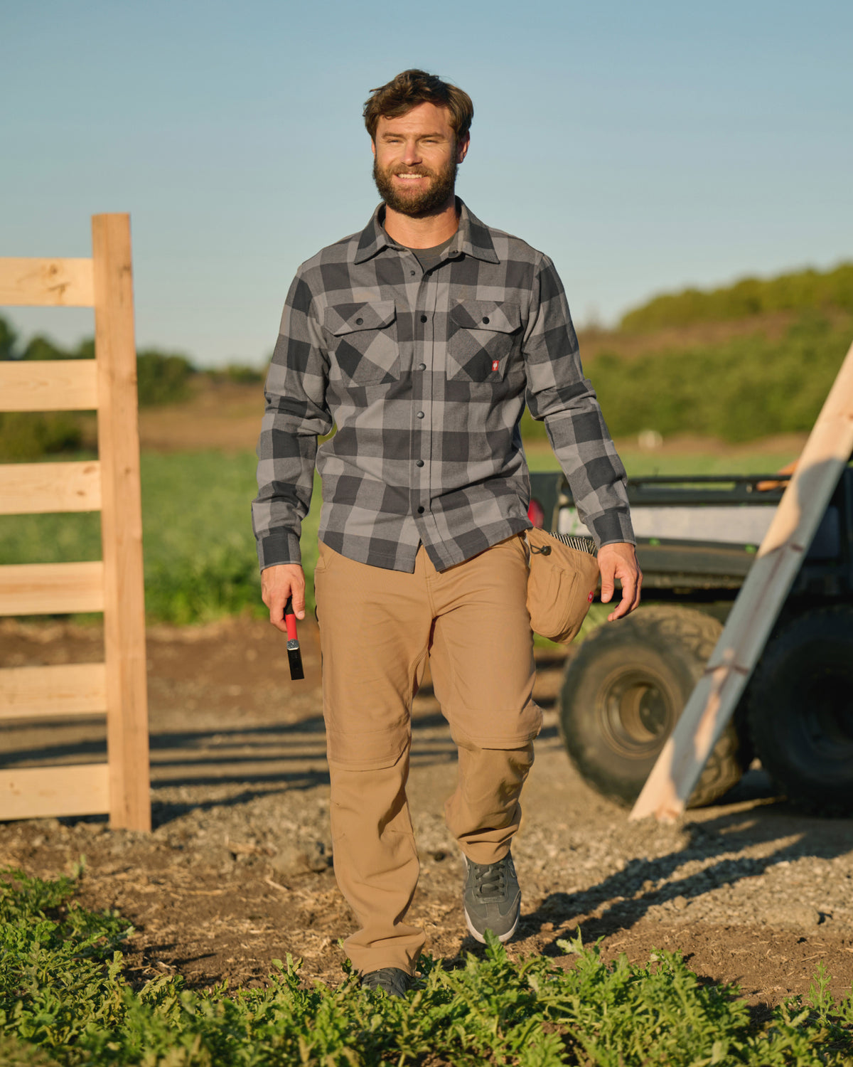 A worker wears the STRAUSS e.s.iconic Flannel Work Shirt in dolphin gray and carbon gray with work pants on a field