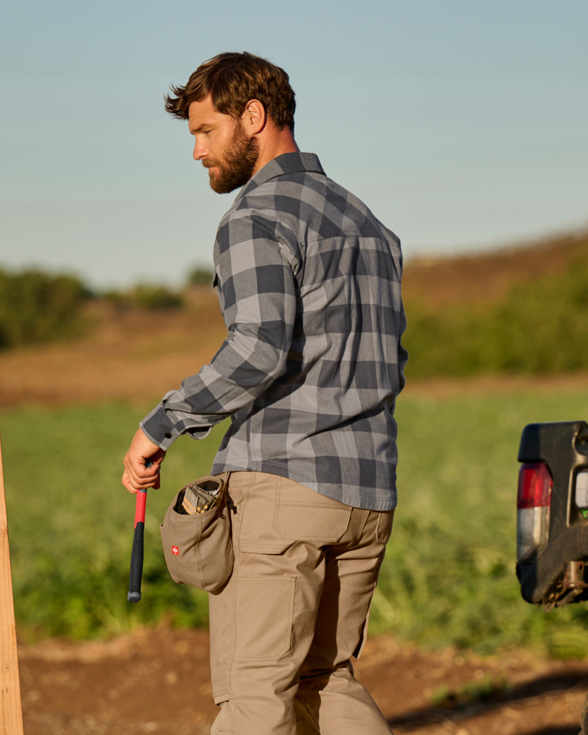 A worker wears the STRAUSS e.s.iconic Flannel Work Shirt in dolphin gray and carbon gray over a T-shirt on a chilly outdoor jobsite