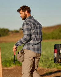 A worker wears the STRAUSS e.s.iconic Flannel Work Shirt in dolphin gray and carbon gray over a T-shirt on a chilly outdoor jobsite