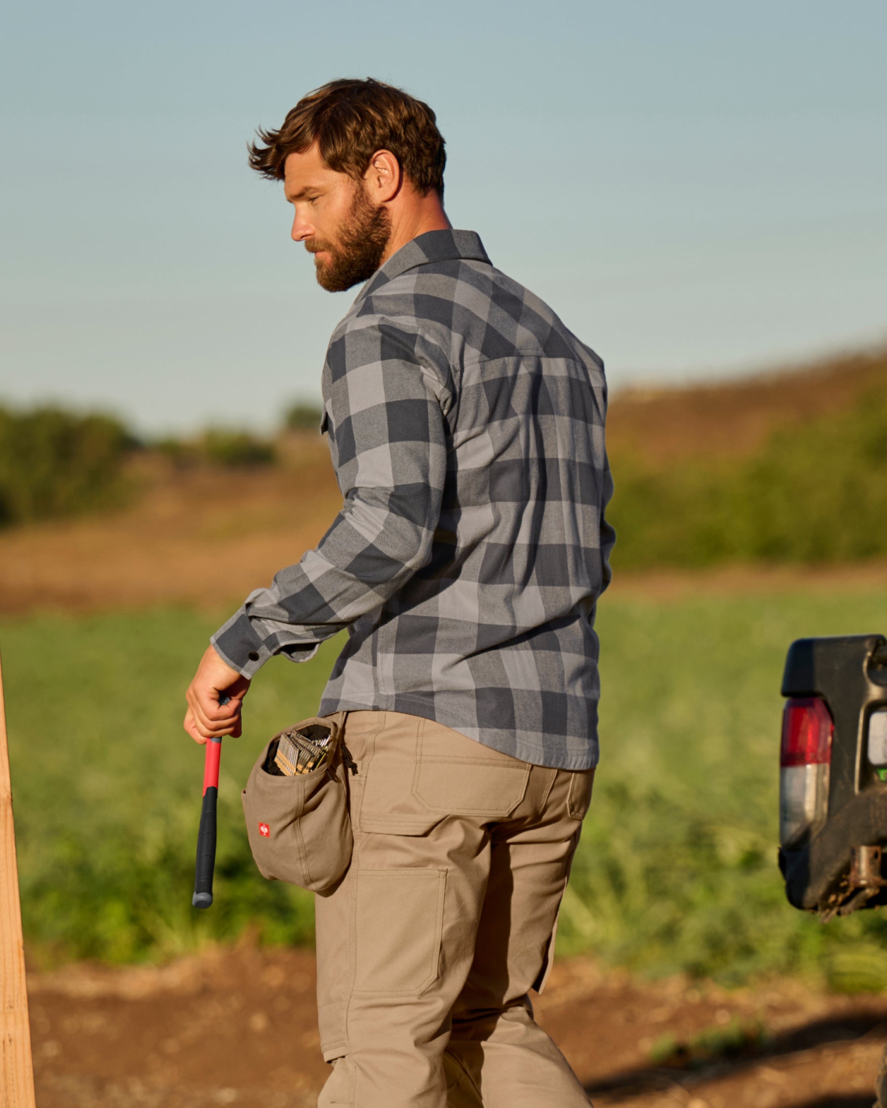 A worker wears the STRAUSS e.s.iconic Flannel Work Shirt in dolphin gray and carbon gray over a T-shirt on a chilly outdoor jobsite