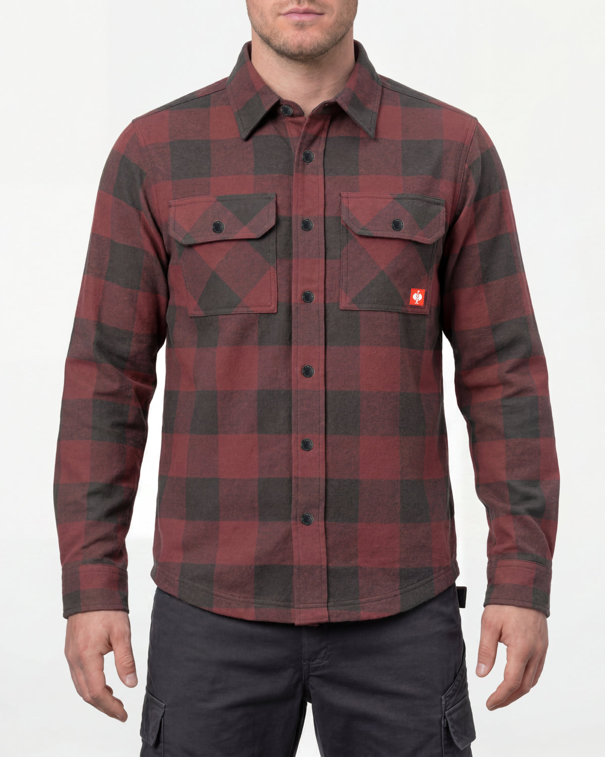 A model wears the STRAUSS e.s.iconic Flannel Work Shirt in oxid red and carbon gray over a T-shirt with work pants and work boots in a studio product scene