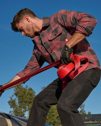 A worker wears the STRAUSS e.s.iconic Flannel Work Shirt in oxid red and carbon gray over a T-shirt with work pantson a jobsite