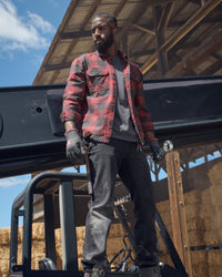 A worker wears the STRAUSS e.s.iconic Flannel Work Shirt in oxid red and carbon gray while being on a farm