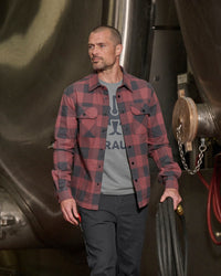 A worker wears the STRAUSS e.s.iconic Flannel Work Shirt in oxid red and carbon gray with work pants on a jobsite