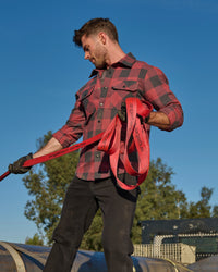 A worker wears the STRAUSS e.s.iconic Flannel Work Shirt in oxid red and carbon gray over a T-shirt on a chilly outdoor jobsite