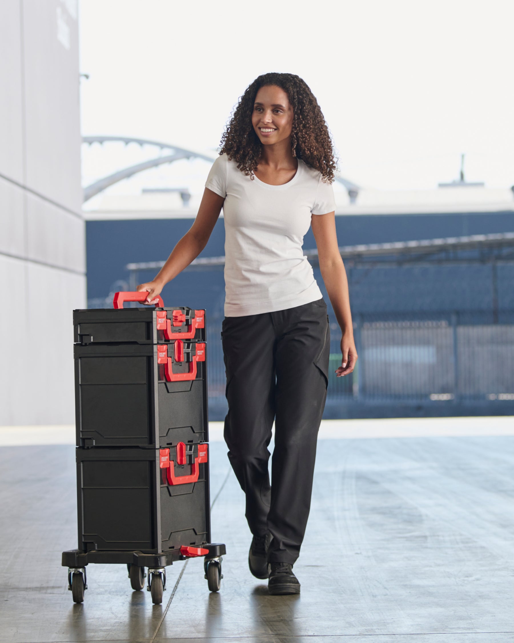 A woman wears the Women's STRAUSS Cotton Stretch T-Shirt in white with work pants in a workshop scene