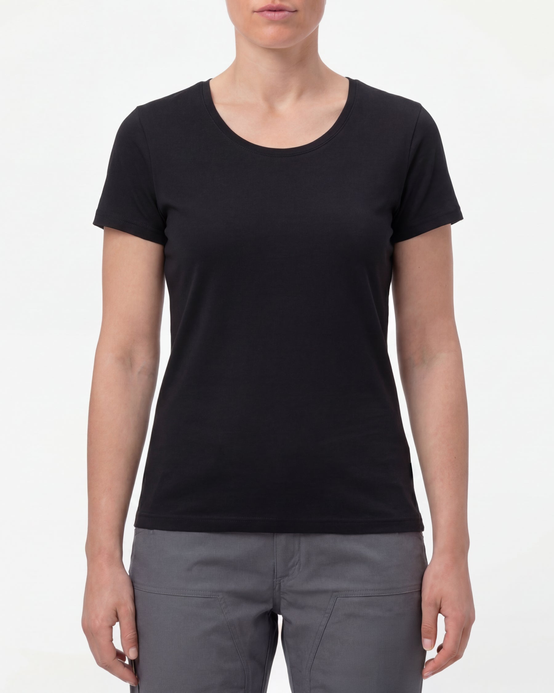 A woman wears the Women's STRAUSS Cotton Stretch T-Shirt in black with work pants and work boots in a studio product scene