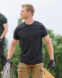 A worker wears the STRAUSS Cotton T-Shirt in black with tan work pants on a sunny jobsite