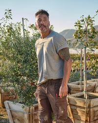 A worker wears the STRAUSS Cotton T-Shirt in gray melange with tan work pants on a sunny jobsite