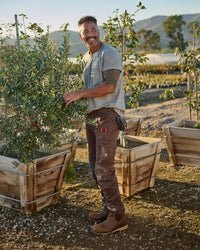 A worker wears the STRAUSS Cotton T-Shirt in gray melange with tan work pants while working in a field