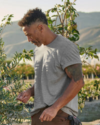 A worker wears the STRAUSS Cotton T-Shirt in gray melange with tan work pants working on a field