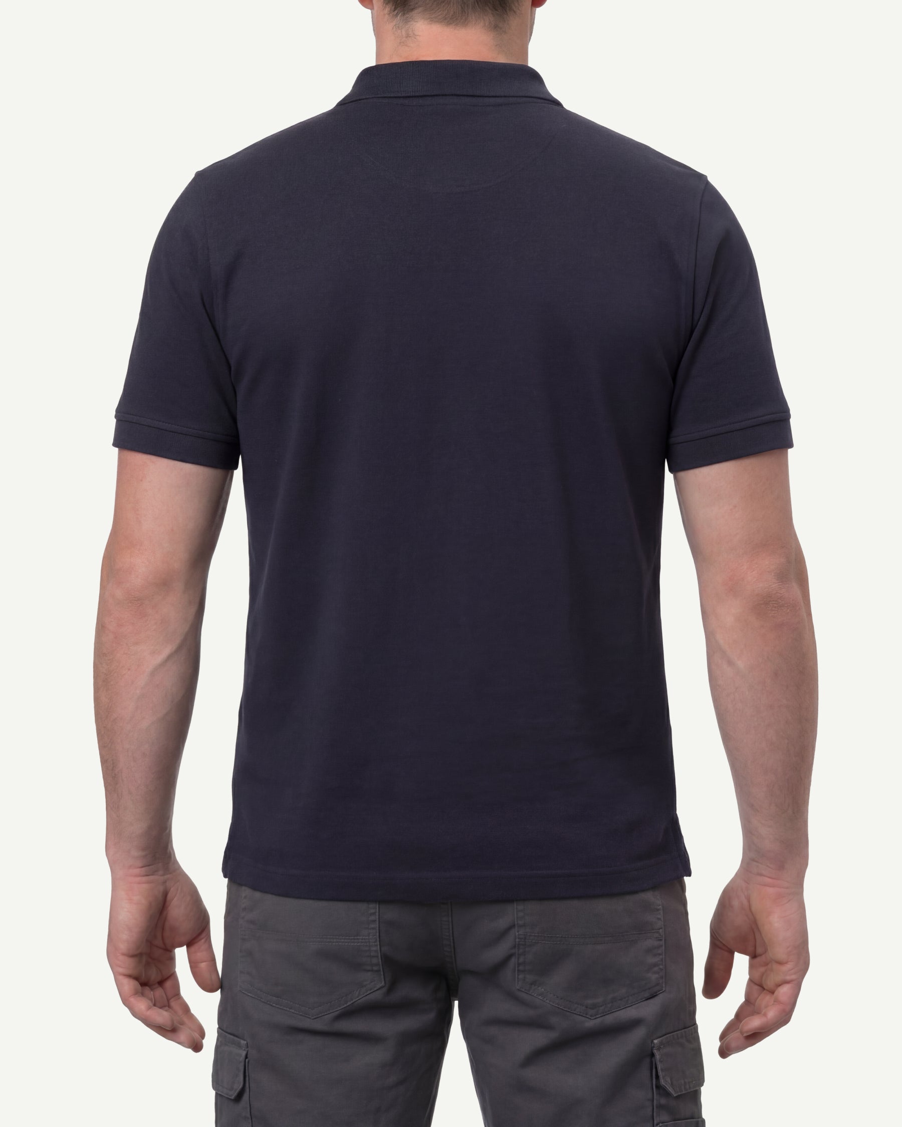 A model wears the STRAUSS Cotton Polo Shirt in nero blue with tan work pants and work boots, showing the shirt fit
