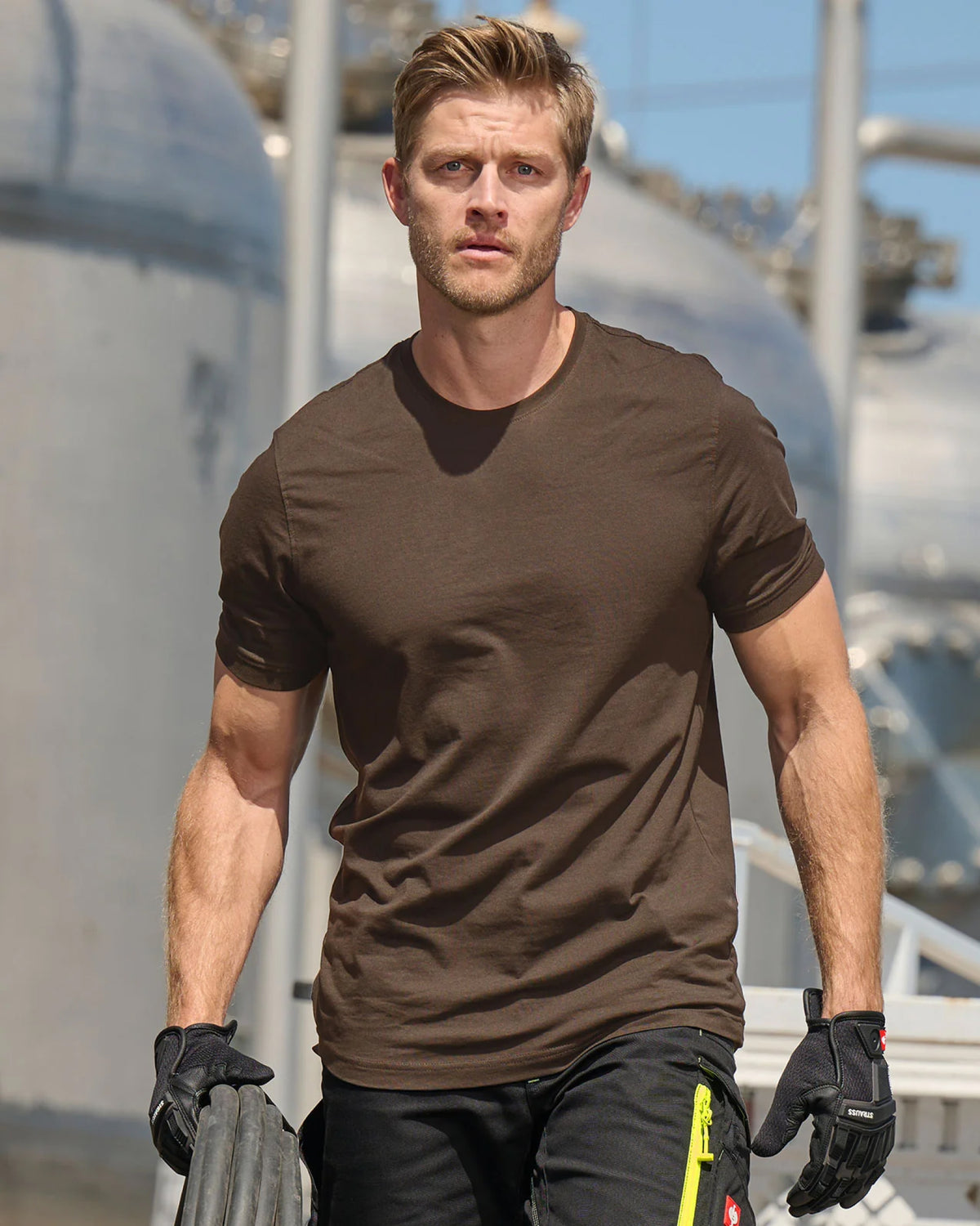 A worker wears the STRAUSS Cotton T-Shirt in hazelnut with tan work pants while working in an industrial setting