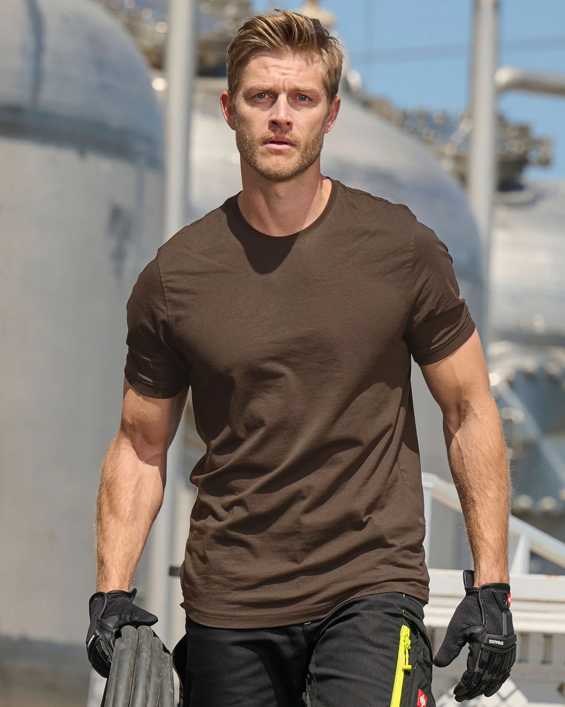 A worker wears the STRAUSS Cotton T-Shirt in hazelnut with tan work pants while working in an industrial setting