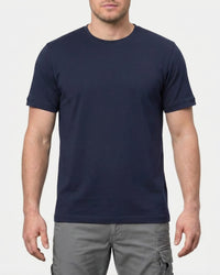 A model wears the STRAUSS Cotton T-Shirt in nero blue with tan work pants and work boots in a studio product scene