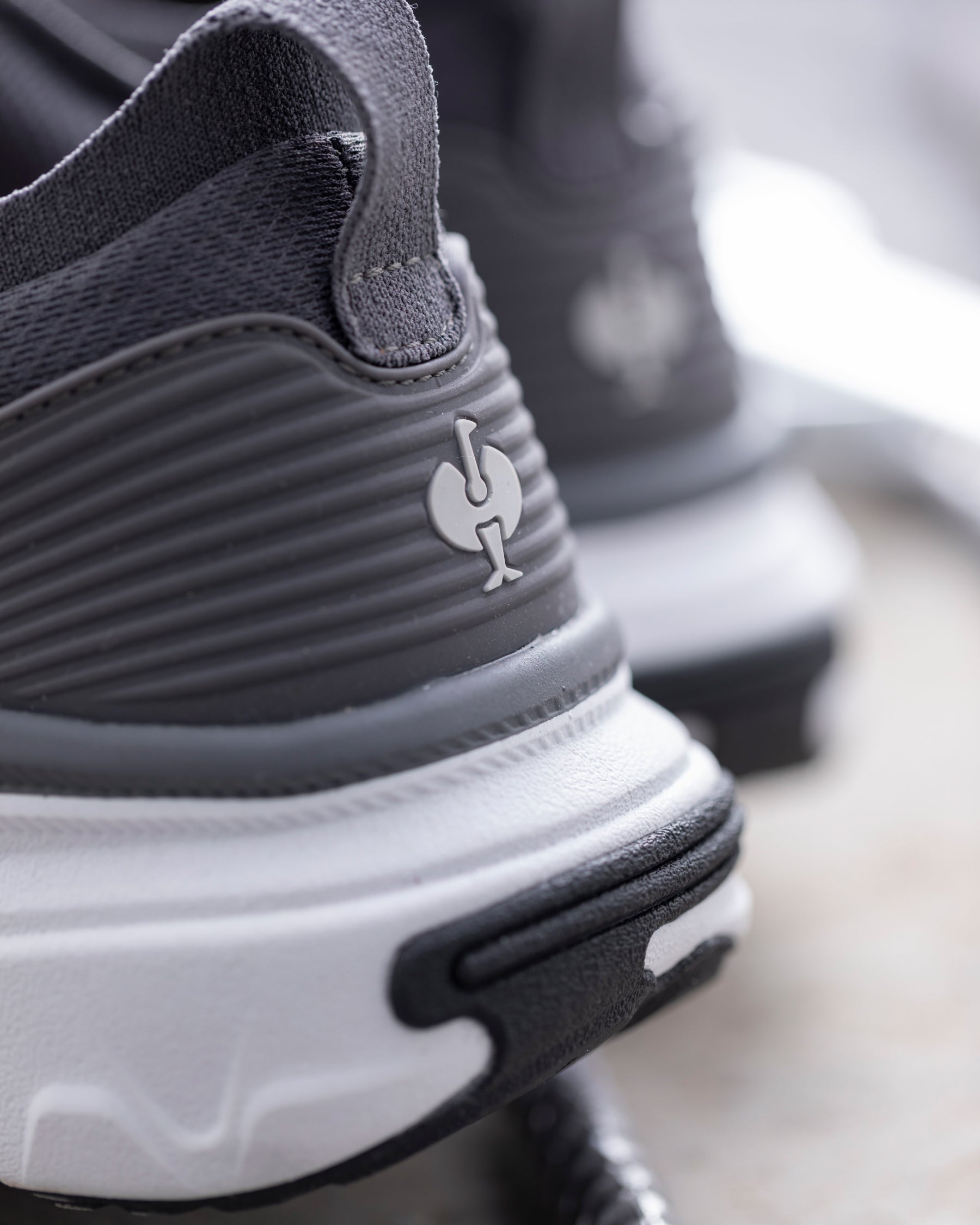 Close-up of a dark gray and white athletic shoe showing the textured side panel, heel logo, and chunky sole.