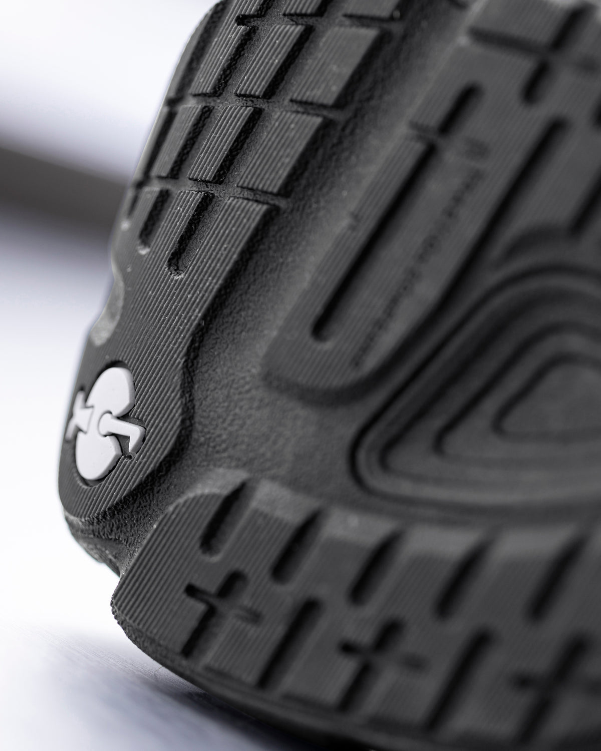 Close-up of a black textured shoe sole with a small white logo, showing detailed tread patterns and molded ridges.